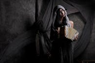 光线昏暗的室内，一名戴着面纱的女子正在演奏手风琴