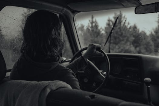 A person driving through a forest in rain, captured in striking grayscale.