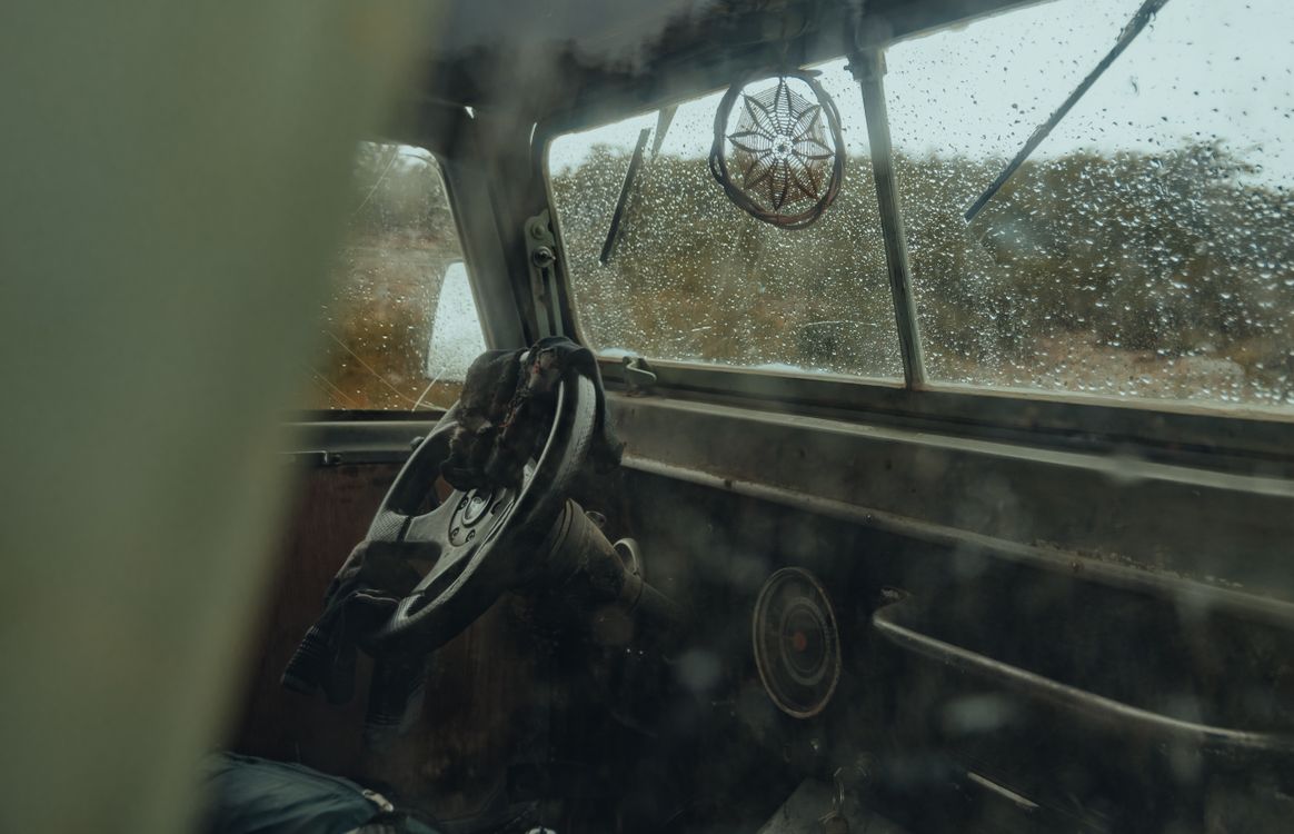 Free Close-up of a vintage car's interior with a focus on the steering wheel and rainy windshield view. Stock Photo