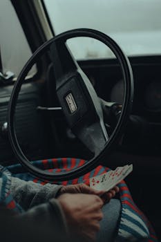 A person sits in a vehicle holding playing cards on a cozy day indoors.