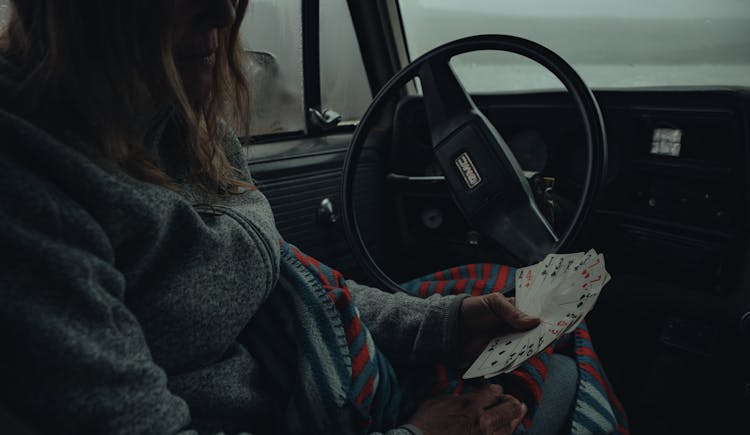 Woman In Gray Jacket Sitting On Driver Seat Holding Playing Cards