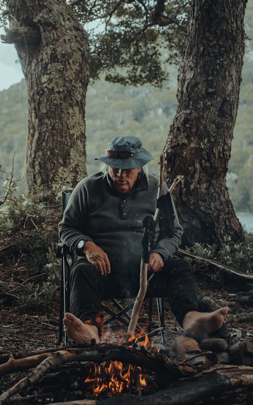 Man Sitting Barefoot next to Campfire 