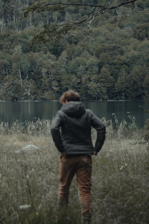 Back View of Person Walking on Grass Field Near Lake