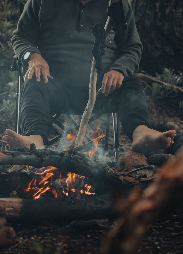 Closeup Of A Man Warming Bare Feet And Drying Socks By A Campfire