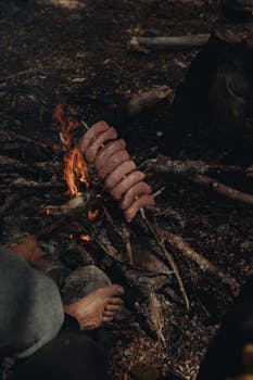 Close-up of sausages roasting over a campfire, creating a cozy outdoor cooking scene.