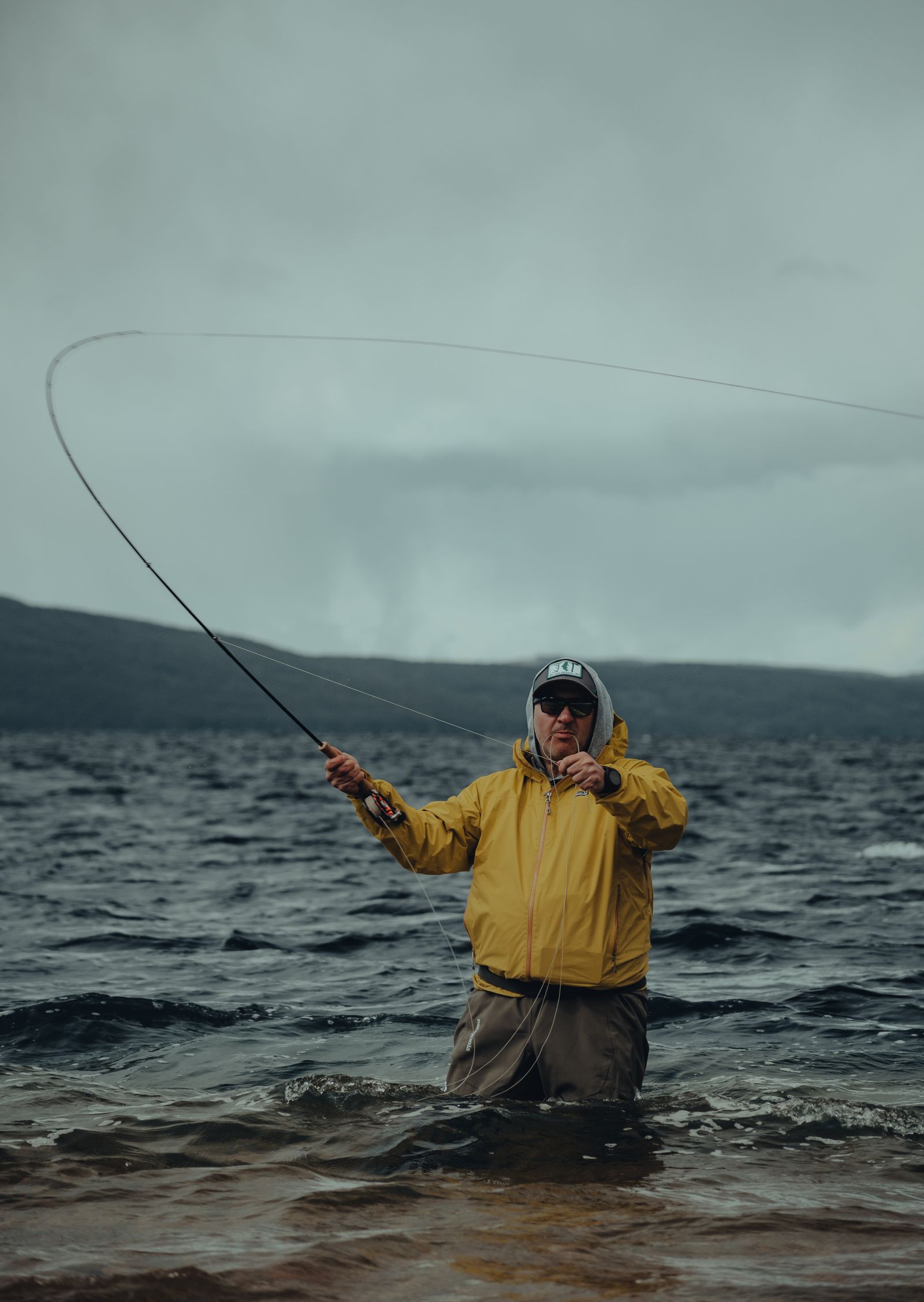 A fly angler loading a fly rod mid-cast, line looping out over a mountain lake
