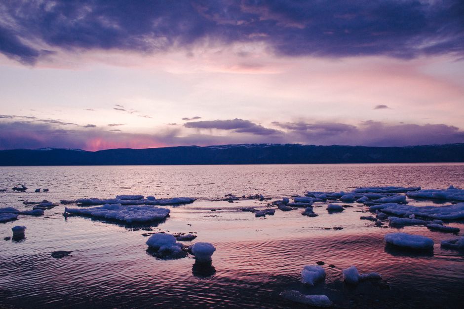 A stunning winter sunset over a serene lake with floating ice and dramatic clouds in the sky.