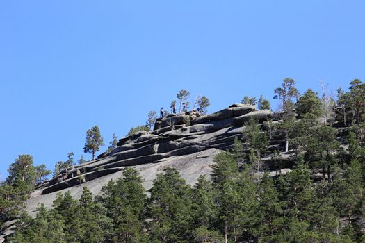 A breathtaking view of people hiking on a rugged rocky mountain under a clear blue sky.