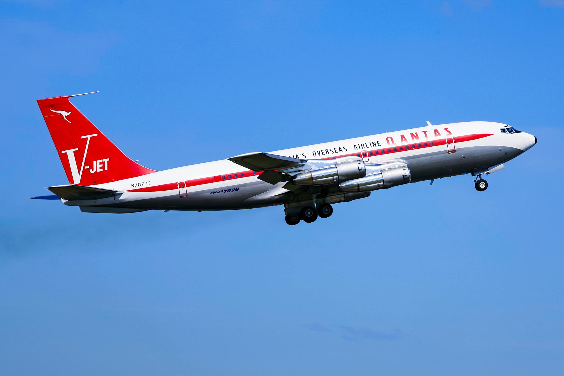 A classic Qantas Boeing 707 jet airliner soaring through the clear blue sky above Sydney.