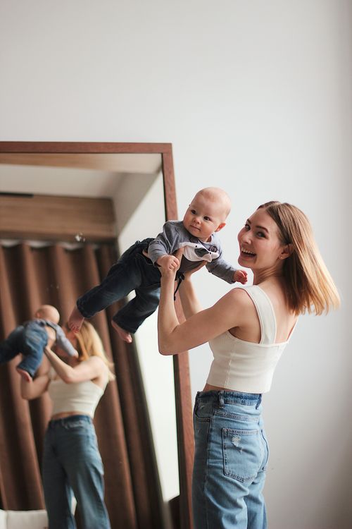 Free A smiling mother plays with her baby, holding him up in front of a mirror indoors. Stock Photo