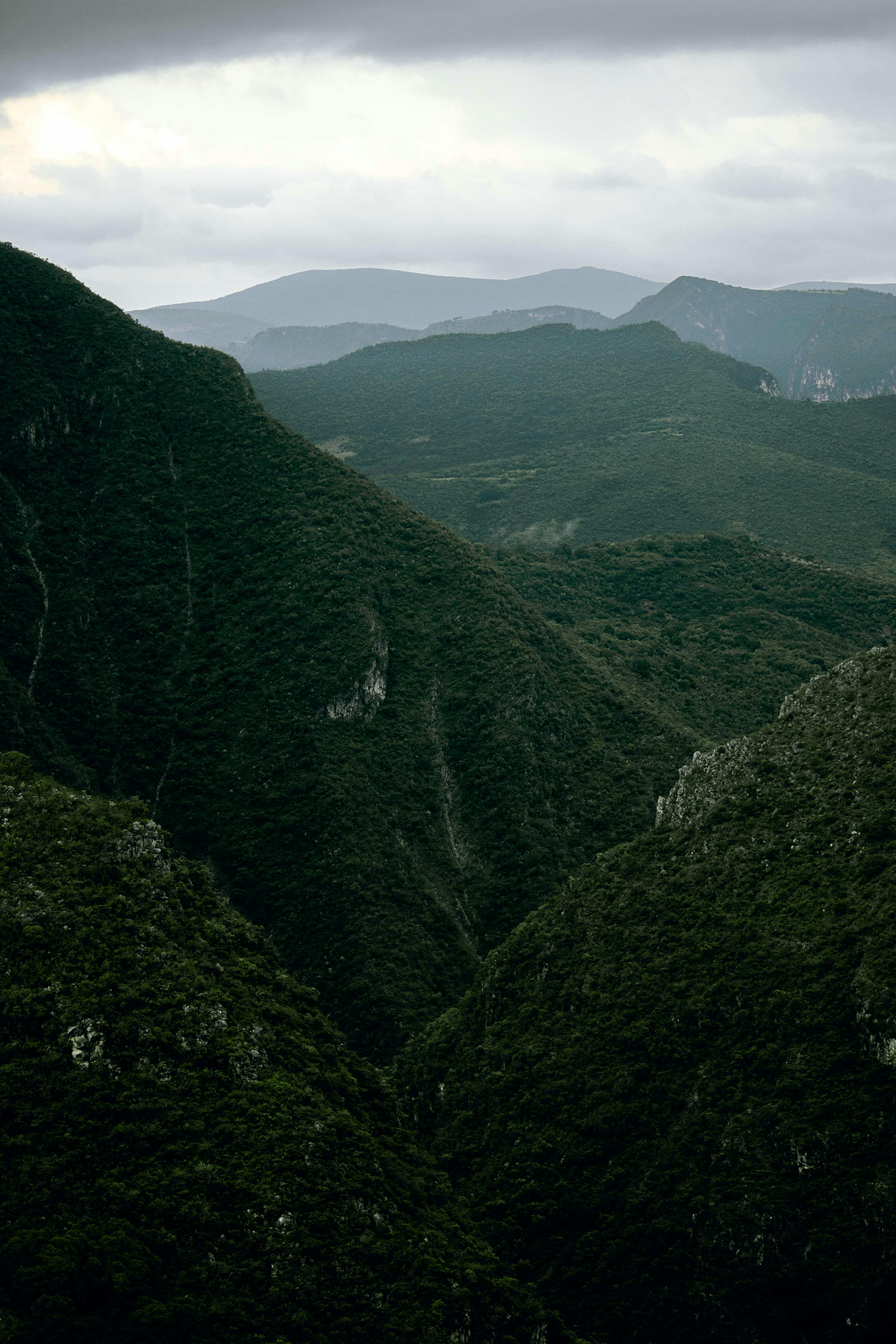 Dramatic view of lush green mountains with cloudy skies, creating a serene and picturesque nature scene.