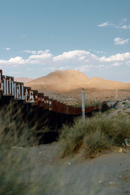 Desert scene with border wall in Ciudad Juárez under a bright sky.