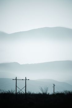 Majestic foggy mountains with silhouetted electric posts in a tranquil setting.