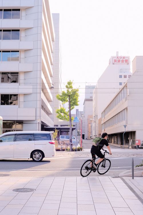 Free A cyclist rides through an urban street at daytime, showcasing city life and transportation. Stock Photo