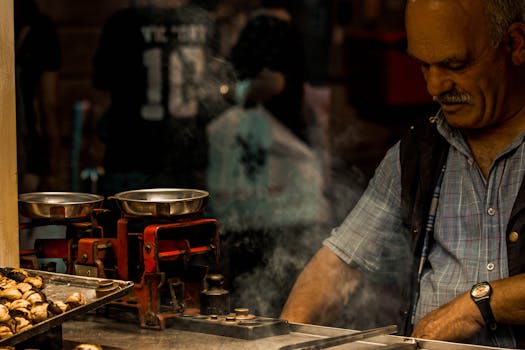 Street vendor grilling chestnuts amidst market smoke with traditional scales in view.
