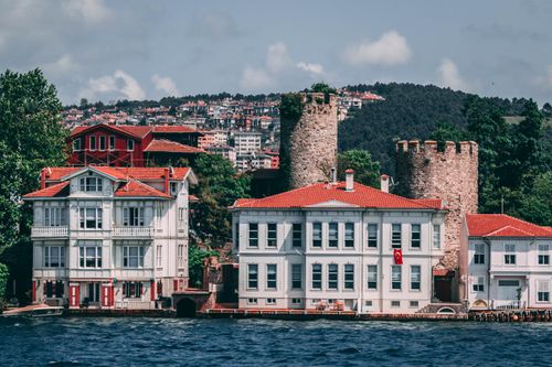 Free Charming waterfront architecture featuring historical stone towers and vibrant red rooftops by the sea. Stock Photo