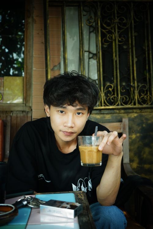 Free A young man holding a glass of iced coffee in a rustic cafe setting with a thoughtful expression. Stock Photo