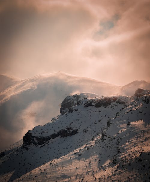 Free Drone Shot of a Cloudy Snow Covered Mountainside
 Stock Photo