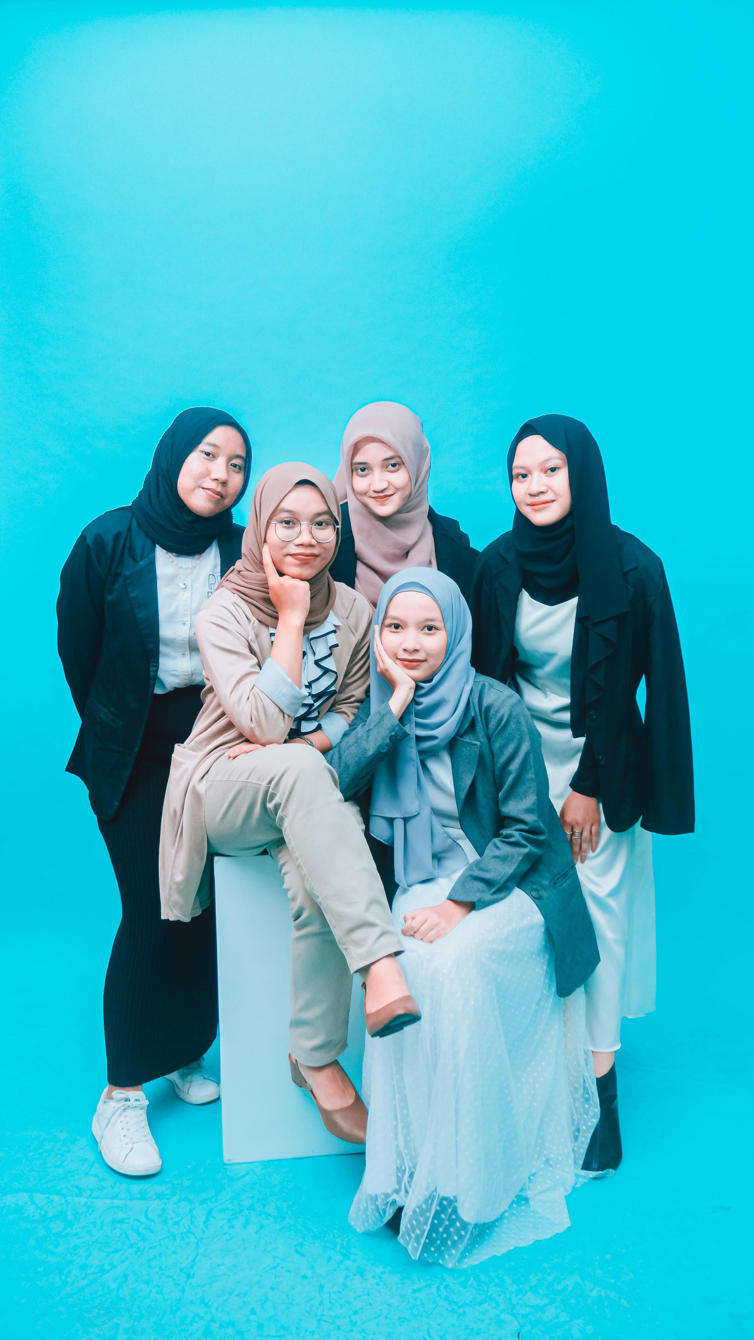 Five women in hijabs posing confidently against a vibrant blue background in a studio shot.