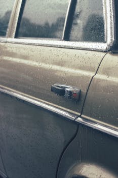 Close-up photo of a car door with raindrops and sleek design details.