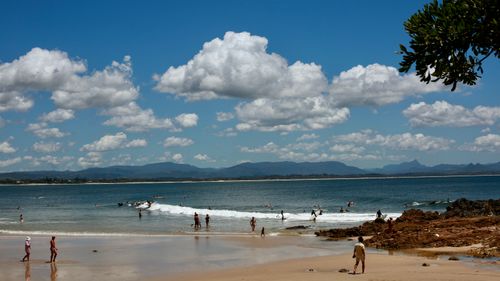 Free A picturesque beach scene with surfers riding the waves under a sky full of white clouds. Stock Photo