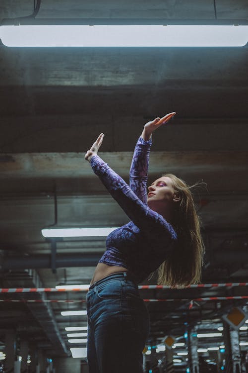 Free Woman in Blue Long Sleeve Shirt and Blue Denim Jeans Raising Her Right Hand Stock Photo
