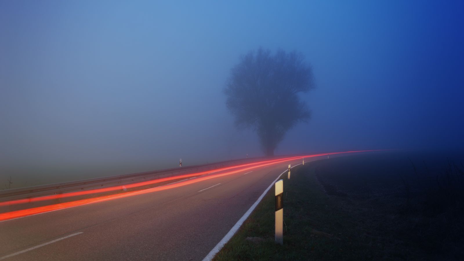 Red taillight trails fading into heavy fog on a rural road at dusk, showing how quickly vehicles ahead disappear