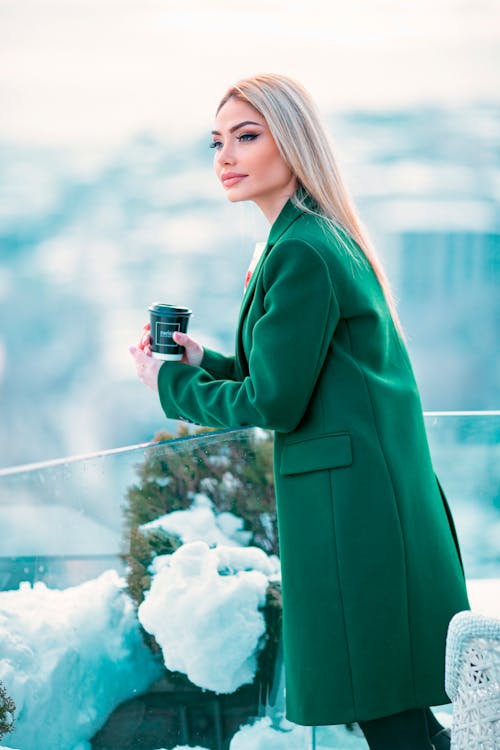 Woman in a Green Coat Holding a Cup of Coffee