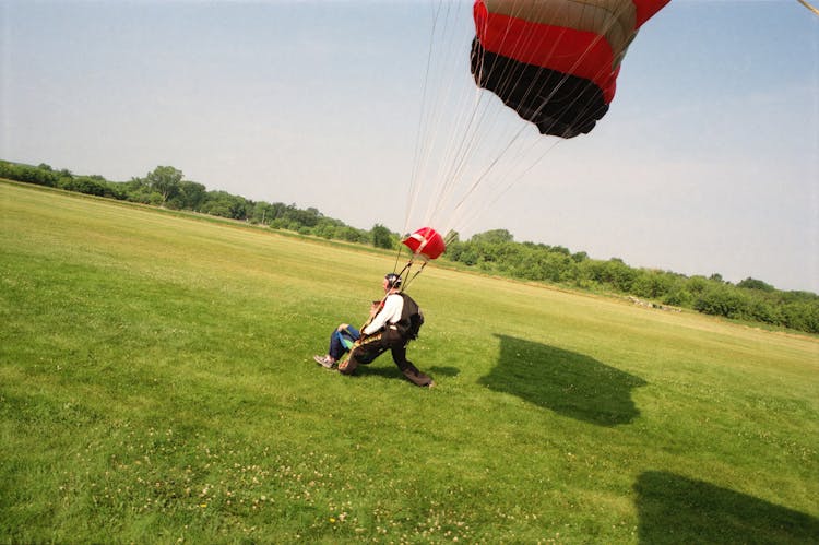 Men In A Parachute Landing In An Open Field