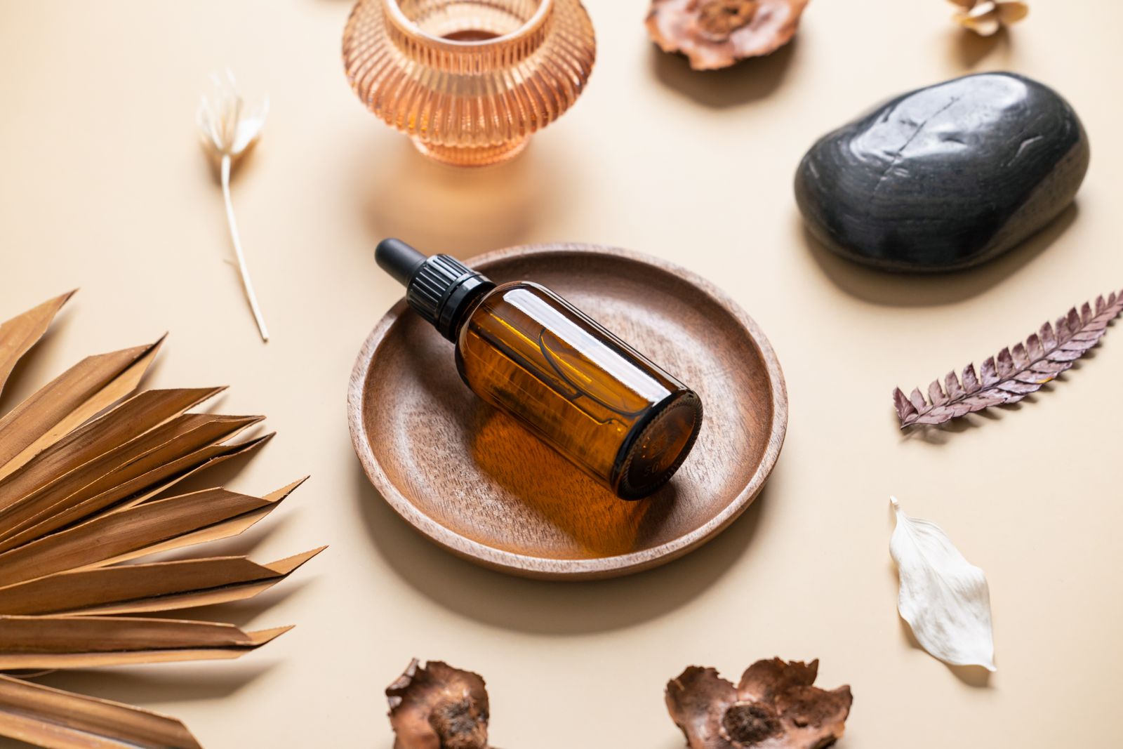 Amber glass dropper bottle resting in a wooden bowl surrounded by dried botanicals and smooth stones.