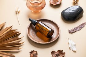Amber glass dropper bottle resting in a wooden bowl surrounded by dried botanicals and smooth stones.