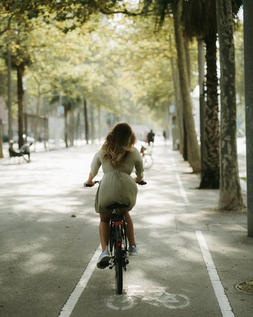 Free Girl in White Long Sleeve Shirt Riding Bicycle on Road Stock Photo