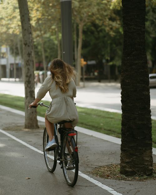 Free A woman riding a bicycle on a tree-lined street in Barcelona, Spain, enjoying a leisurely day outdoors. Stock Photo
