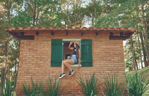 Free A Woman Posing on a Window of a Brick Building Stock Photo