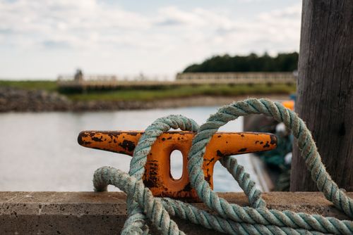 Free Detailed close-up of a weathered rope wrapped around an orange bollard at a Canadian harbor. Stock Photo