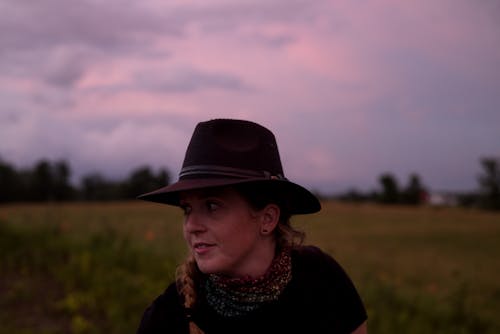 Free Woman in Black Hat and Black Shirt Standing on Green Grass Field Under White Clouds during Stock Photo