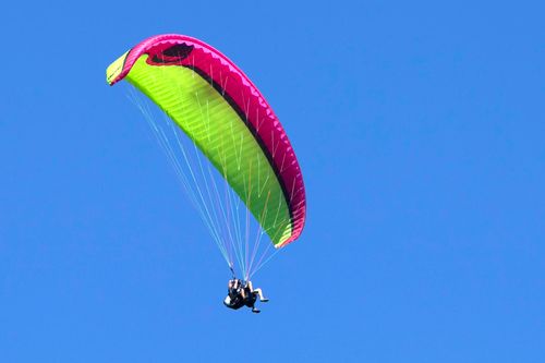 Free Brightly colored paraglider in flight against a clear blue sky, capturing the thrill of adventure. Stock Photo