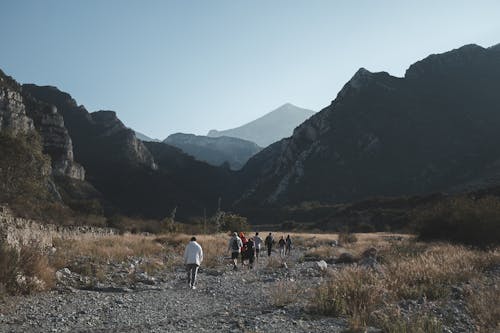 Group of People Walking on Rocky Ground Near Mountains 