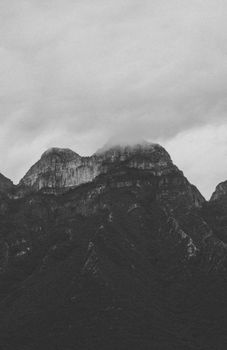 Grayscale image of a majestic mountain range enveloped by clouds, creating a dramatic natural scene.
