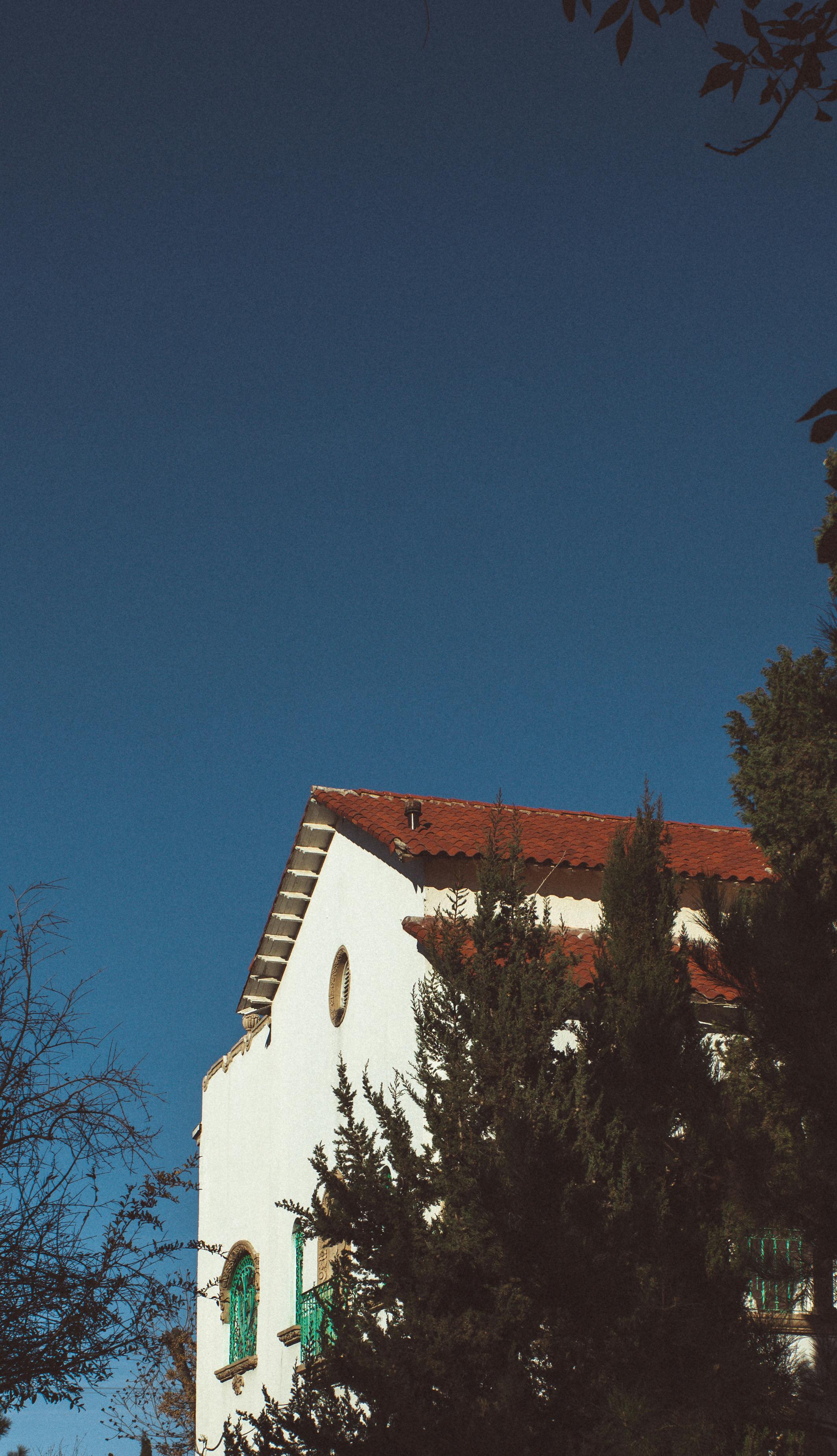 A picturesque white house with red roof surrounded by lush trees under a clear blue sky.
