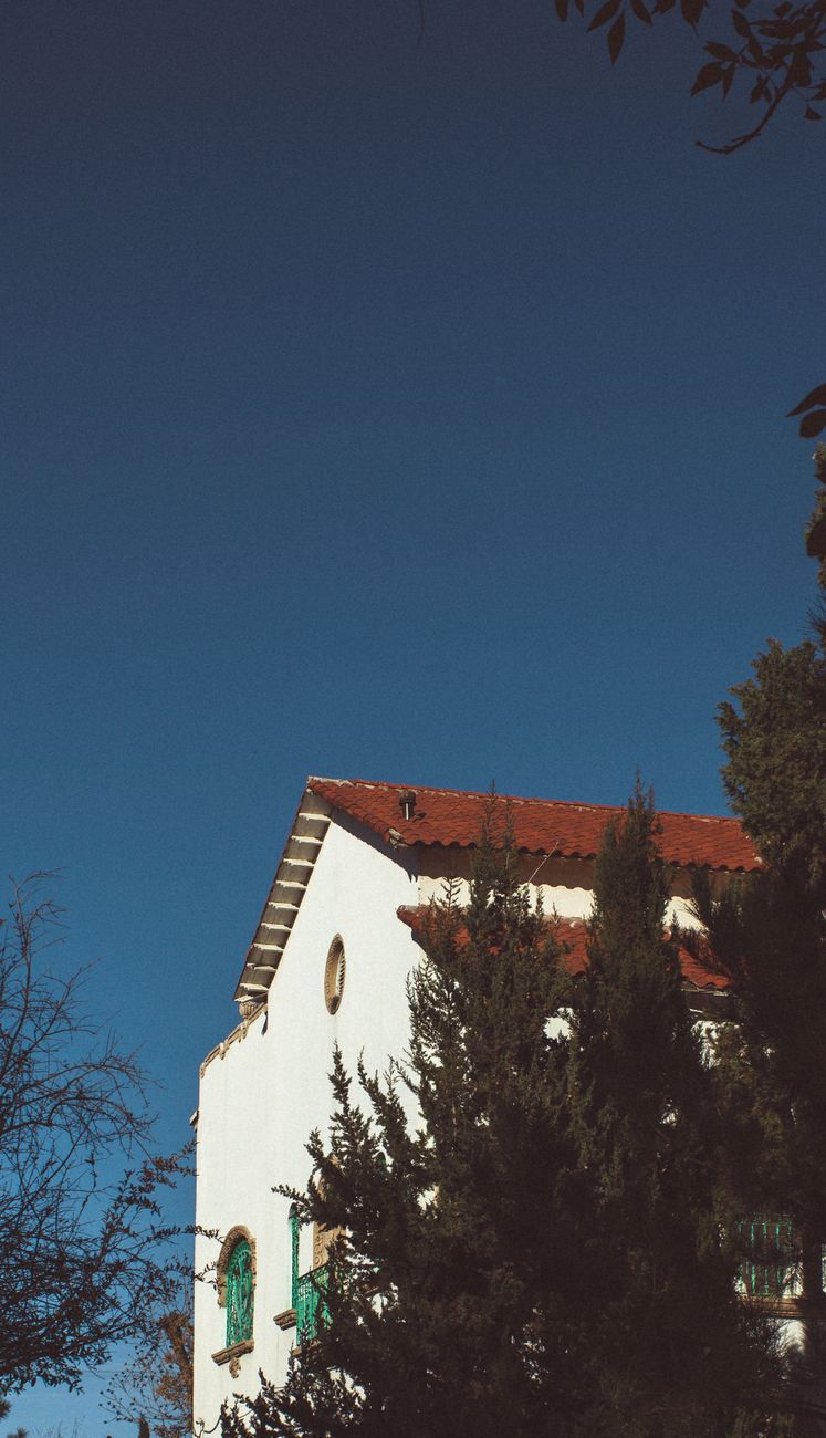 A picturesque white house with red roof surrounded by lush trees under a clear blue sky.