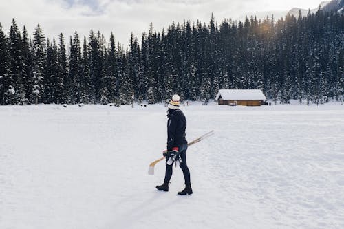 Photo of a Woman Holding Hockey Sticks while Walking on Snow