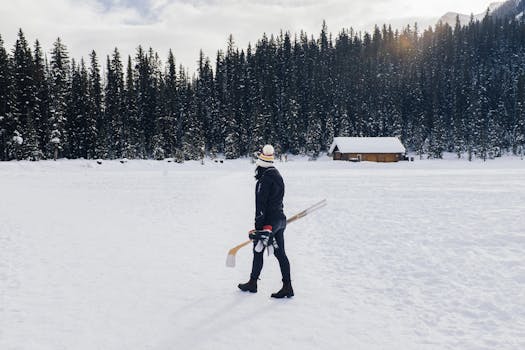 A woman in winter attire walking on snowy Lake Louise with hockey gear.