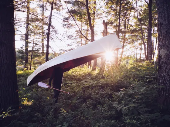 A paddler carrying a canoe overland on a portage trail