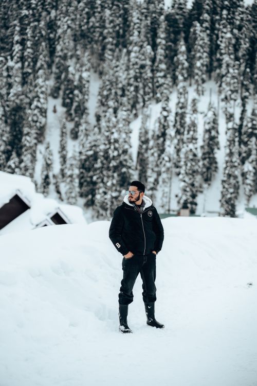 Free Man wearing black jacket and sunglasses stands on a snowy landscape with trees. Stock Photo
