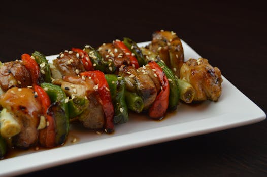 Close-up of grilled chicken skewers with bell peppers and sesame seeds on a white plate, perfect for a tasty meal.