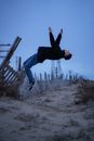 Man in Black Jacket and Blue Denim Jeans Jumping on Brown Wooden Fence