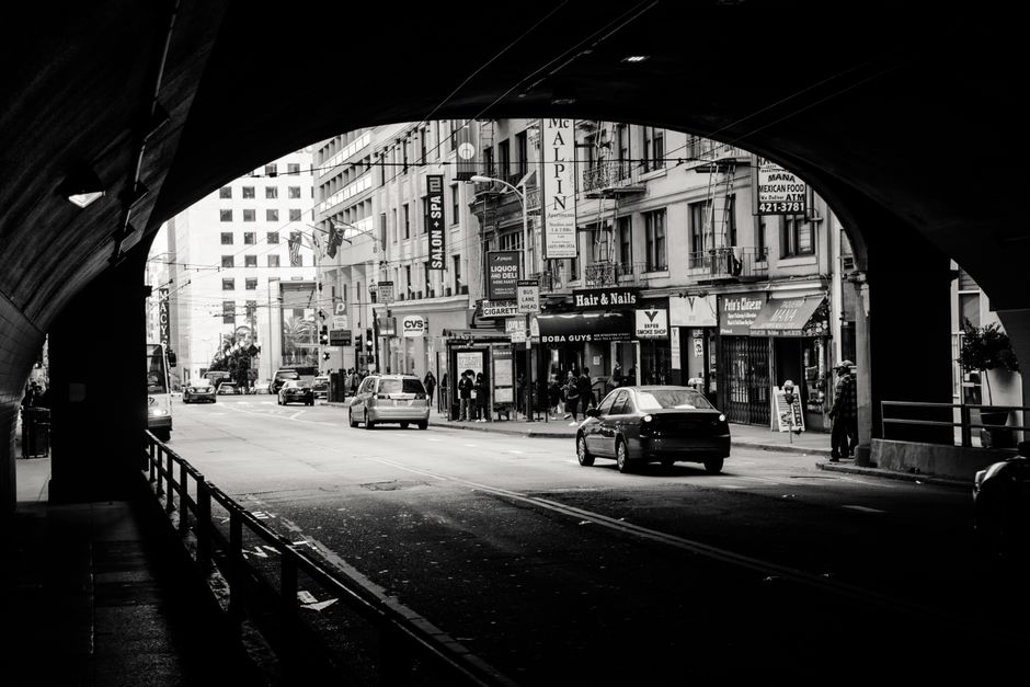 Black and white photo of a city street with cars and pedestrians seen through a tunnel.