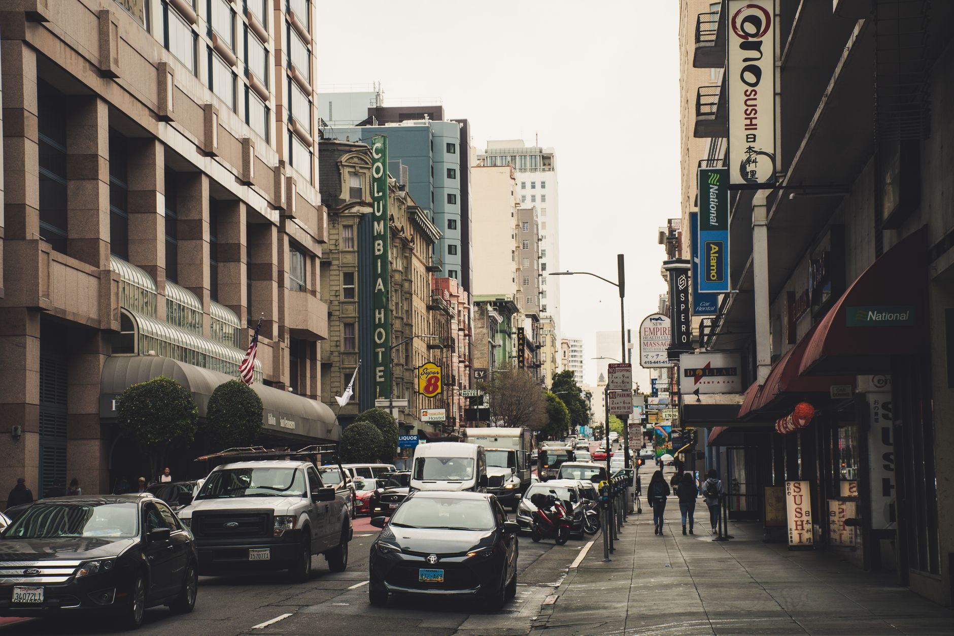 Vibrant city street filled with vehicles and pedestrians amid towering buildings and diverse signage.
