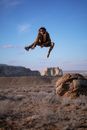 Man in Black Jacket Jumping on Brown Rock